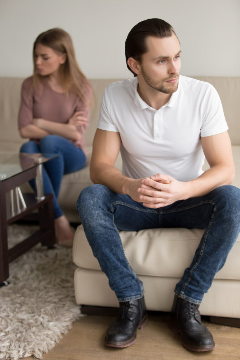 Two adult partners sitting apart on a sofa during a difficult moment