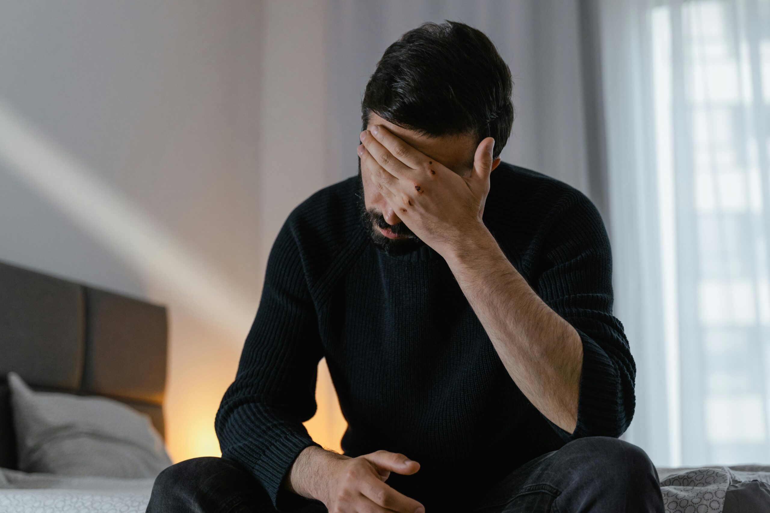 Man sitting on the edge of a bed with his hand covering his face, showing emotional distress and fatigue, symbolizing the struggle with fentanyl addiction