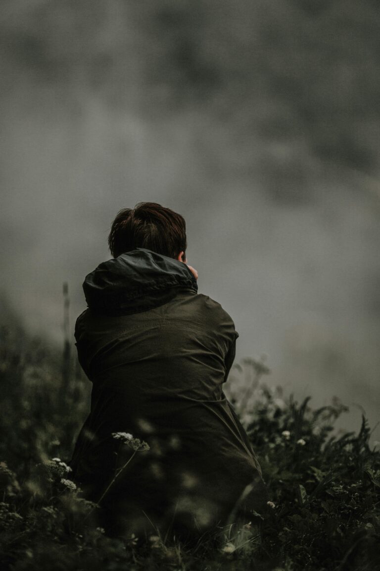 Adult seated outdoors facing a misty landscape