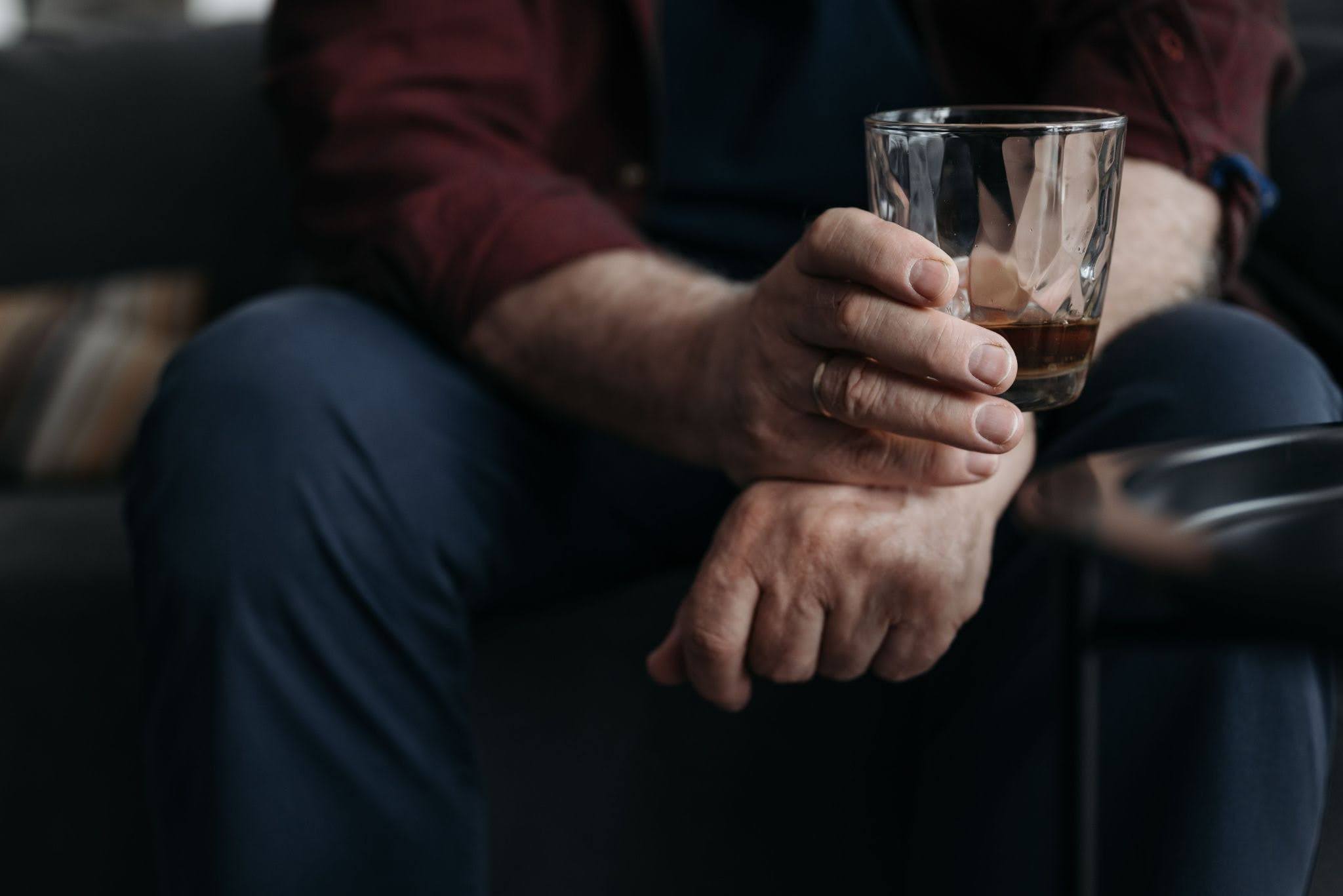 Person holding a glass of alcohol while seated at home, illustrating alcohol cravings at night