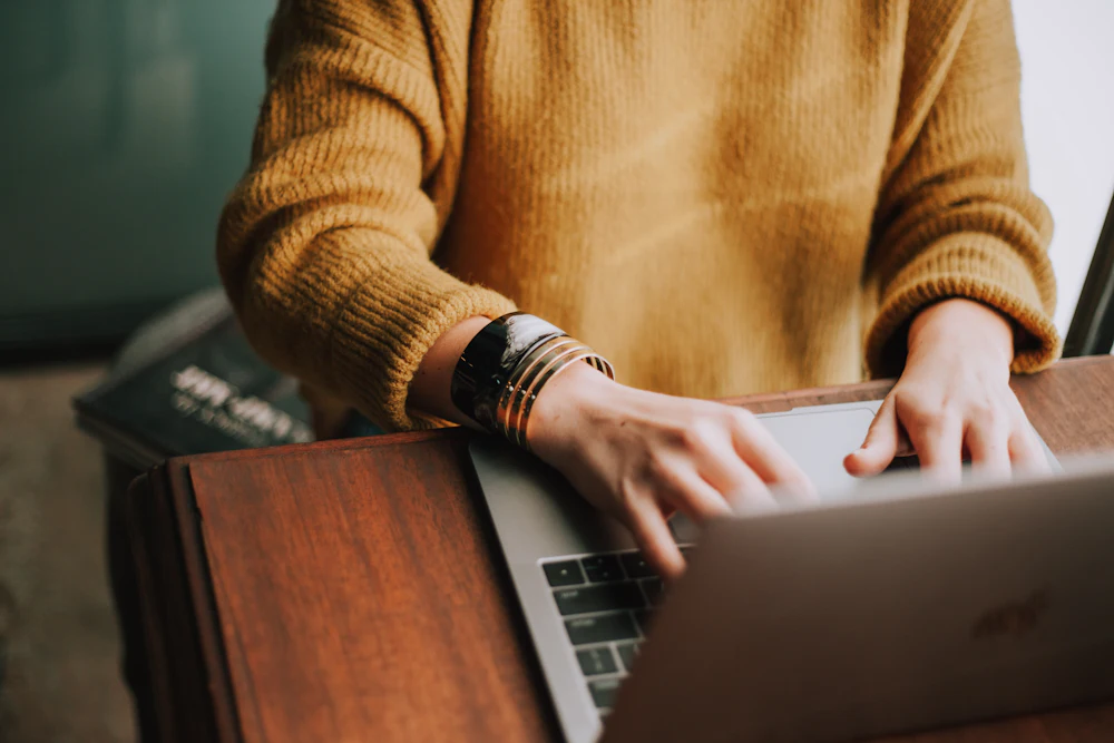 Hands typing on a laptop at a wooden desk, with no face visible