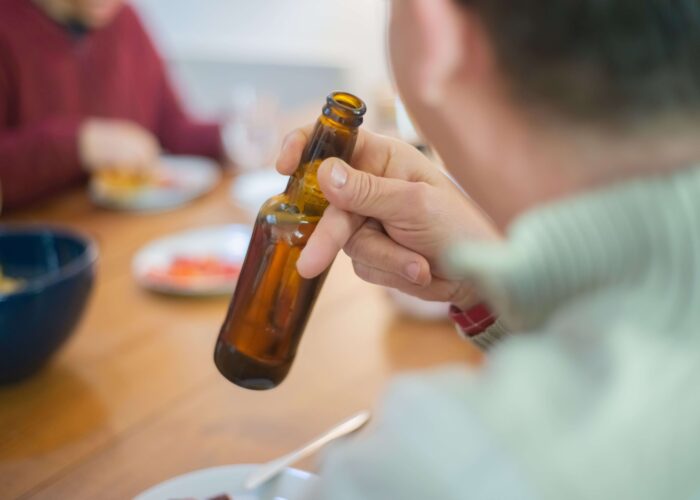 Person holding a beer bottle while drinking with others, highlighting the challenges of staying sober when your partner still drinks.