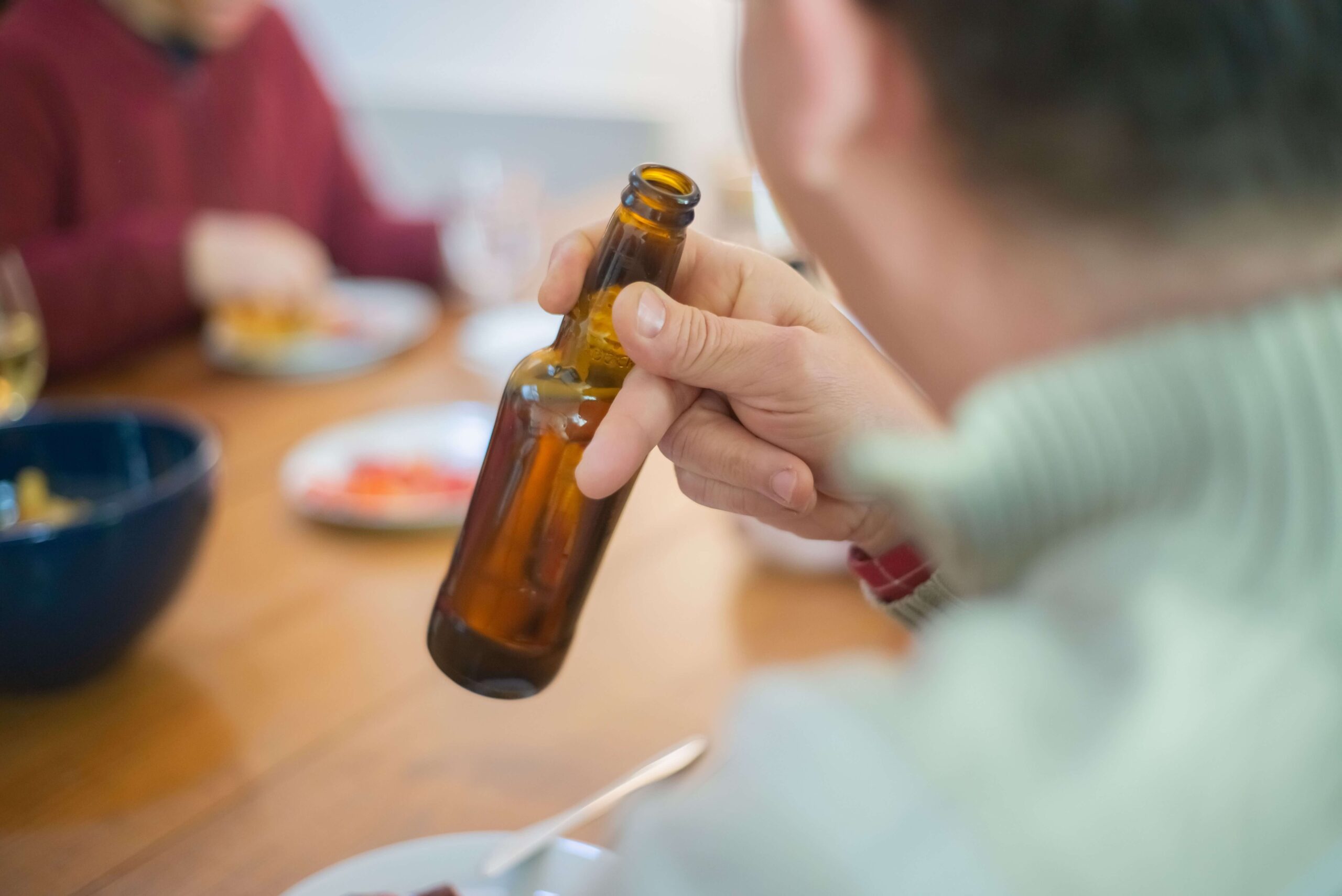 Person holding a beer bottle while drinking with others, highlighting the challenges of staying sober when your partner still drinks.
