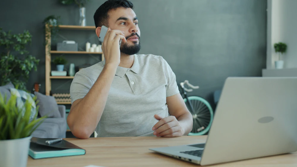 A man talking on his phone while seated at a table at home