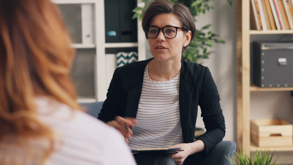An adult speaking with a counselor who is holding a clipboard