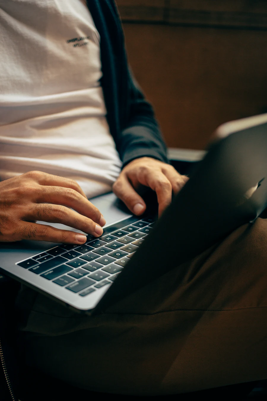 Close-up of hands using a laptop while seated, with no face visible